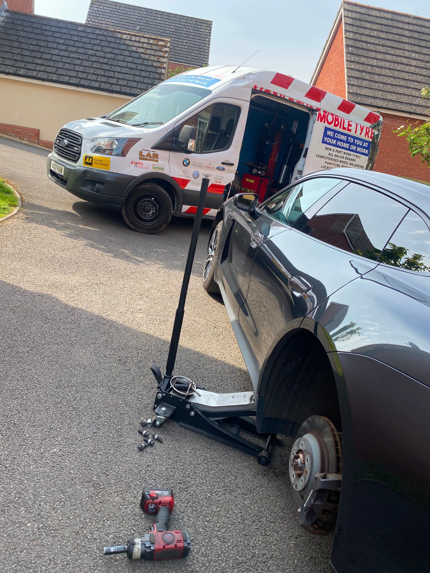 Tyre valve and wheel nut work on a customer vehicle — wheel off, hardware laid out beside the trolley jack
